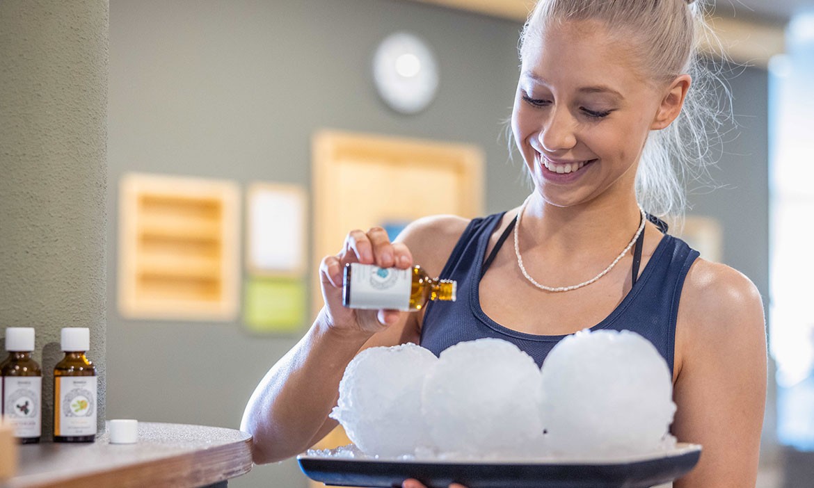 Eine freundliche Mitarbeiterin der Saunawelt Ishara bereitet einen aromatischen Aufguss vor, indem sie duftendes Öl auf große Eiskugeln träufelt. Die Kombination aus Eis und ätherischen Ölen sorgt für ein erfrischendes Saunaerlebnis in entspannter Atmosphäre.