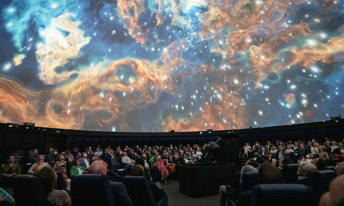 Eine beeindruckende Projektion eines Nebels im Planetarium, während das Publikum gespannt nach oben blickt. Die Kuppel verwandelt sich in ein Fenster zum Universum.