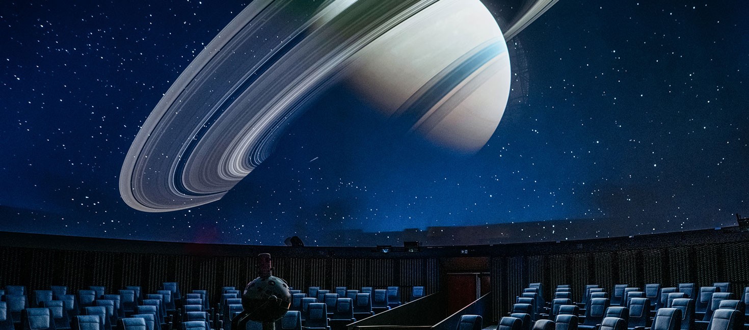 Der majestätische Saturn mit seinen Ringen füllt die Kuppel des Planetariums. Die leeren Sitze warten auf Besucher, die sich auf eine faszinierende Reise durch das All begeben.