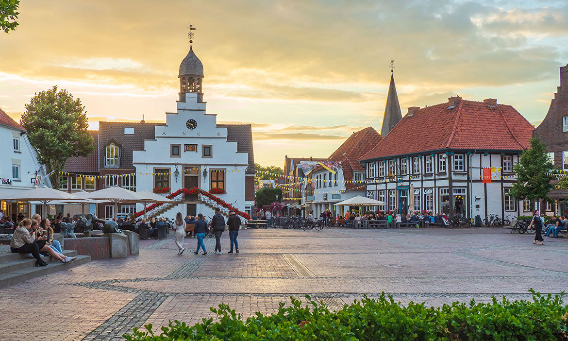Abendstimmung auf dem Lingener Marktplatz mit historischem Rathaus, Fachwerkhäusern, vielen Menschen auf dem Platz und Außengastronomie.