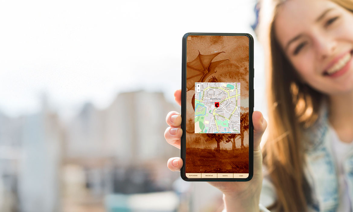 Eine junge Frau hält ein Smartphone in die Kamera, während ihr Gesicht und der städtische Hintergrund unscharf bleiben. Auf dem Display ist eine App mit sepiafarbener Gestaltung zu sehen; in der Mitte wird ein Kartenausschnitt mit einem roten Standortmarker angezeigt. Unten im Bildschirm stehen die Menüpunkte „Aufgaben“, „Inventar“, „Karte“ und „Chat“. Im Hintergrund sind unscharfe Gebäude und heller Himmel zu erkennen.