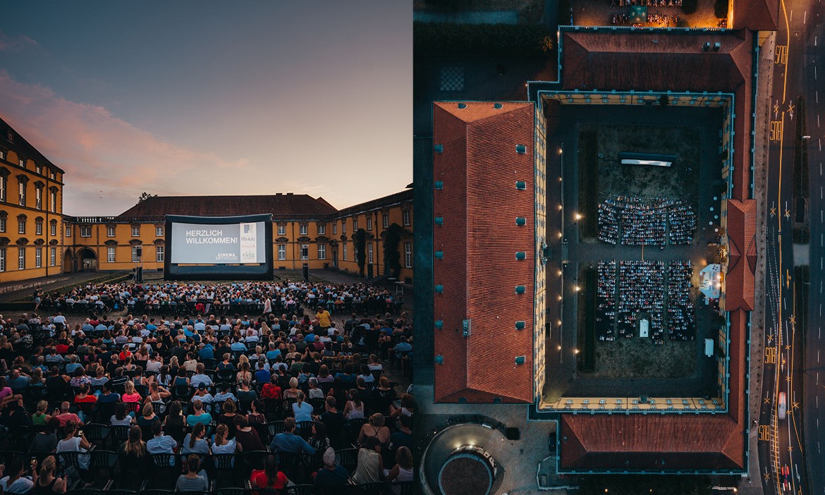 Zweiteilige Ansicht eines Open-Air-Kinos im Innenhof eines historischen Schlosses. Links sitzen viele Besucherinnen und Besucher vor einer großen Leinwand, auf der „Herzlich willkommen“ steht. Rechts ist dieselbe Veranstaltung aus der Vogelperspektive zu sehen: Der rechteckige Schlosshof ist von Gebäuden umgeben und mit Stuhlreihen gefüllt.
