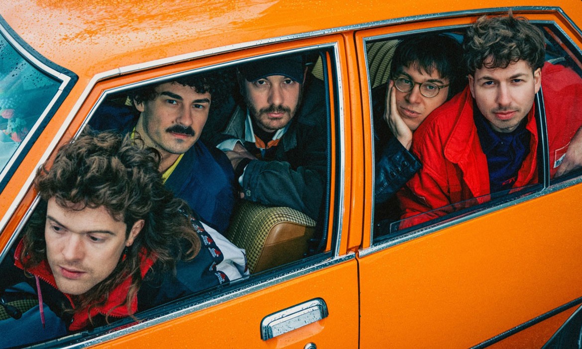 Die fünf Mitglieder der Indie-Pop-Band Von Wegen Lisbeth sitzen dicht gedrängt in einem orangefarbenen Auto und schauen durch die geöffneten Seitenfenster nach draußen.