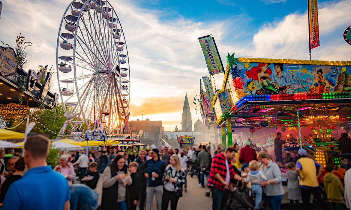Gut besuchte Herbstkirmes in Rheine mit Riesenrad, Karussell und Kirchturm im Hintergrund.