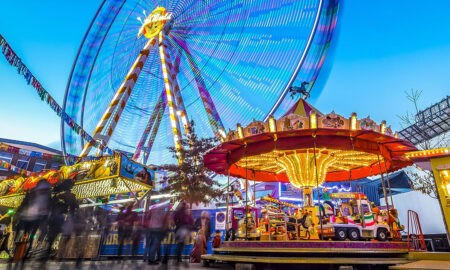 Bunt beleuchtetes Riesenrad und Kinderkarussell auf einem gut besuchten Jahrmarkt.