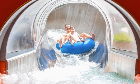 Ein Mann und ein Kind rutschen lachend auf einem blauen Doppelreifen aus einer Wasserrutsche im Nettebad Osnabrück.